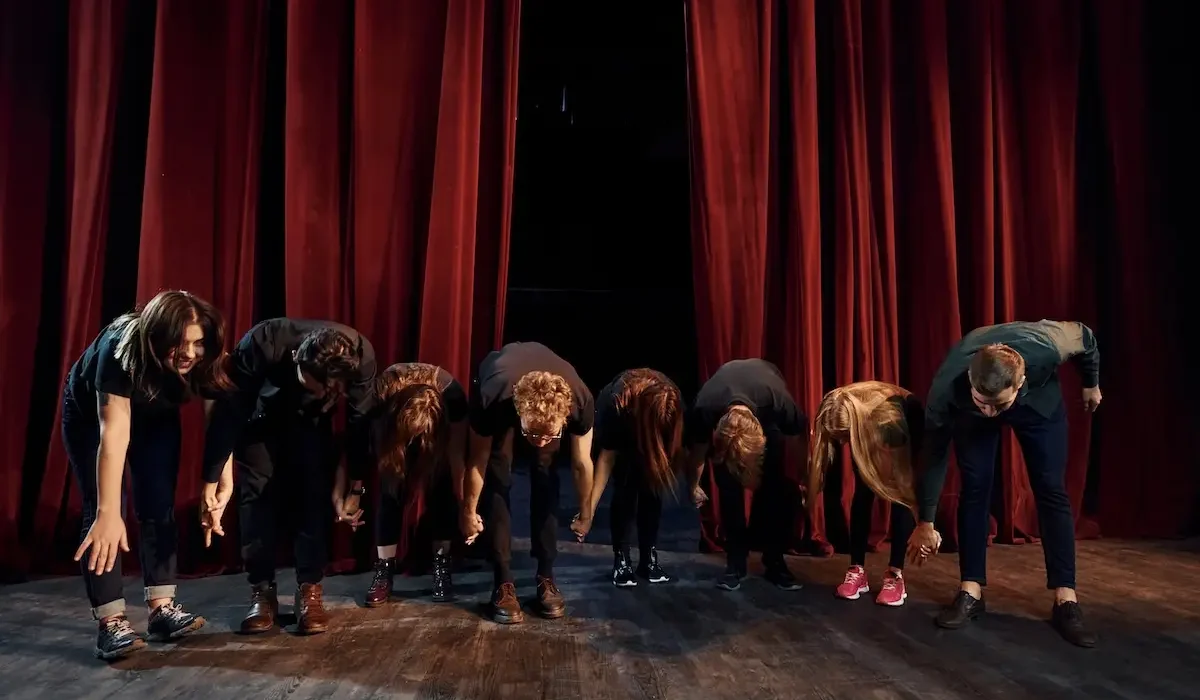 People bowing to audience. Group of actors in dark colored clothes on rehearsal in the theater People bowing to audience. Group of actors in dark colored clothes on rehearsal in the theater.