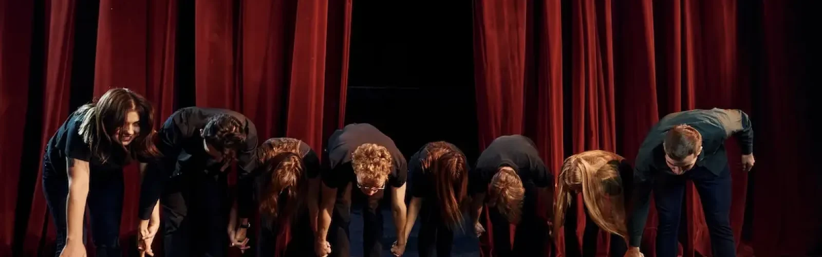 People bowing to audience. Group of actors in dark colored clothes on rehearsal in the theater.
