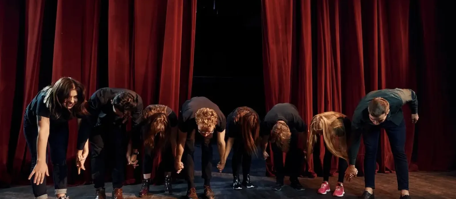 People bowing to audience. Group of actors in dark colored clothes on rehearsal in the theater People bowing to audience. Group of actors in dark colored clothes on rehearsal in the theater.
