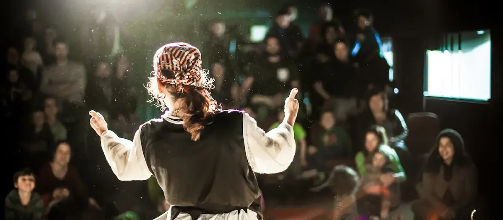 Comedy pirates perform on stage A performing arts entertainer is seen from the back in selective focus, dressed as a pirate on stage during a comedy act with blurry audience at back.