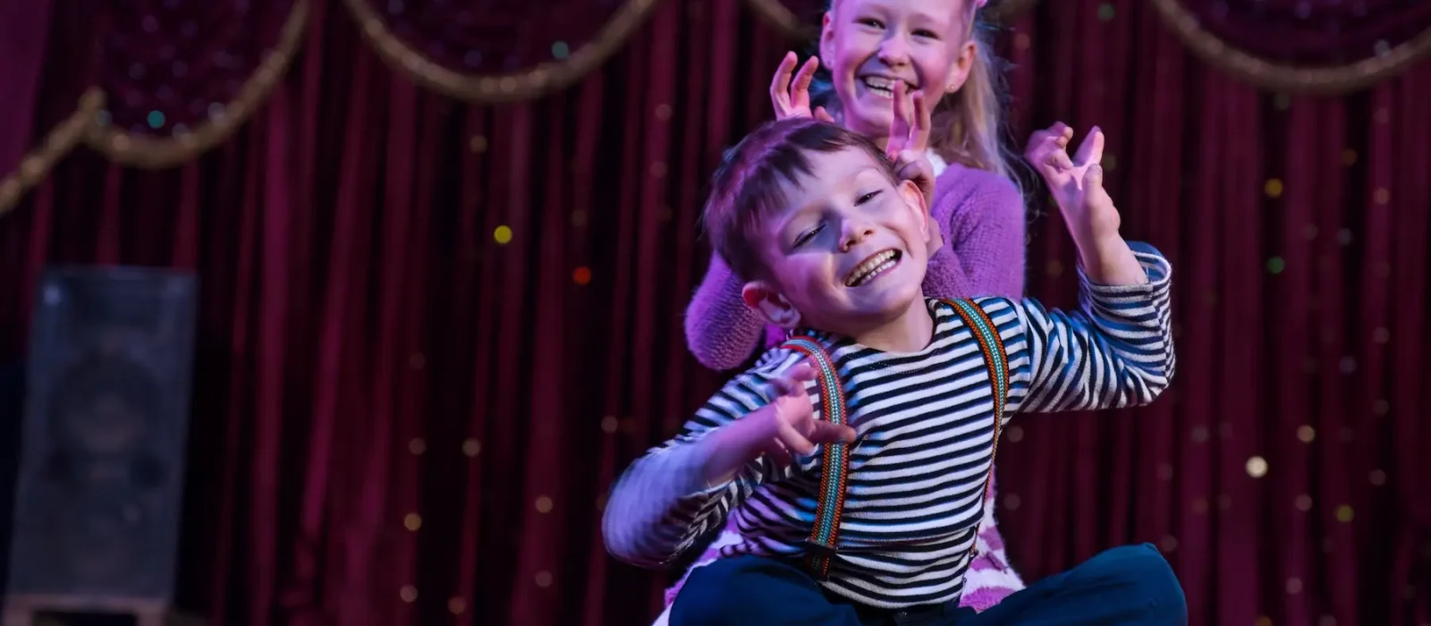 Two funny children acting as monsters on stage Two funny playful children, boy and girl, smiling while acting as monsters with claws, on a purple stage, in a theatrical representation